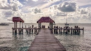 A wooden pier leading to a thatched-roof structure with a view of the sea and boats in the distance. - Deluxe Double Room at Casa de los Sueños (Isla Mujeres)