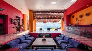 A vibrant lounge area with a view of the ocean, featuring a central table and multiple seating options. - Deluxe Double Room at Casa de los Sueños (Isla Mujeres)