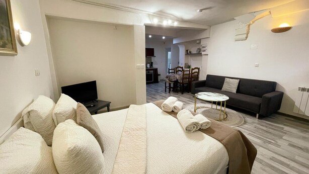 Une chambre d’hôtel avec un lit, une télévision, un canapé, un coin repas et une cuisine à l’arrière-plan.