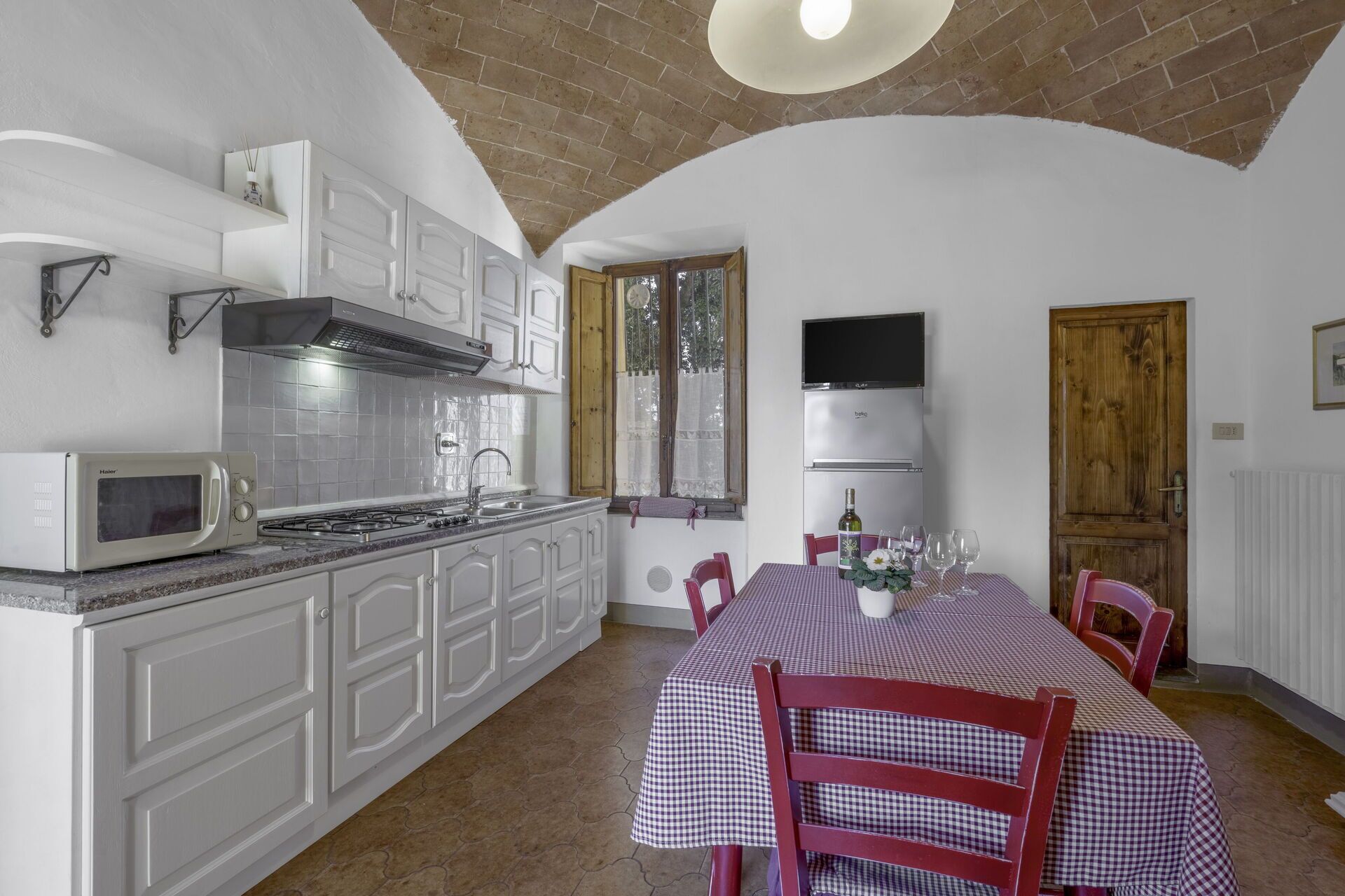 A compact kitchen with white cabinetry, a microwave, a stove, and a sink. There's a dining table with a checkered tablecloth and red chairs.