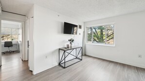 Una habitación amplia y luminosa con un ventanal grande, un televisor montado y un mueble consola minimalista.