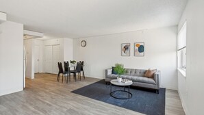 Un salon moderne avec un canapé gris, une table basse ronde et un coin repas comprenant une table et des chaises.