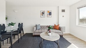 A modern living room with a sofa, a glass dining table with chairs, a coffee table, and two abstract paintings on the wall. - Legacy at Imperial Village 516 I 2 Bed 2 Bath (Ric hmond)