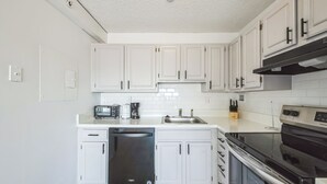 A modern kitchen with white cabinets, a black dishwasher, a stove, and a sink. - Legacy at Imperial Village 516 I 2 Bed 2 Bath (Ric hmond)