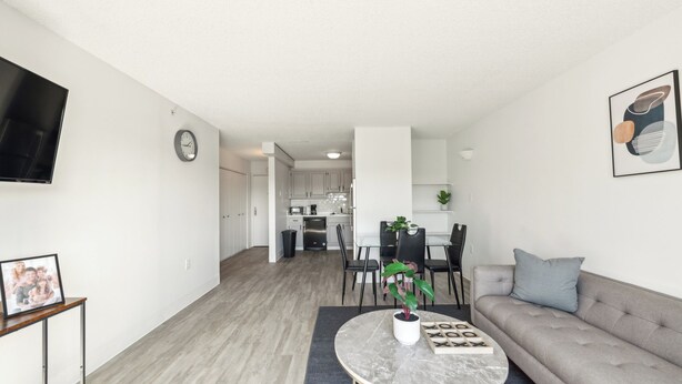 A modern living room with a sofa, a coffee table with a plant, and a dining area with chairs and a table. - Legacy at Imperial Village 516 I 2 Bed 2 Bath (Ric hmond)