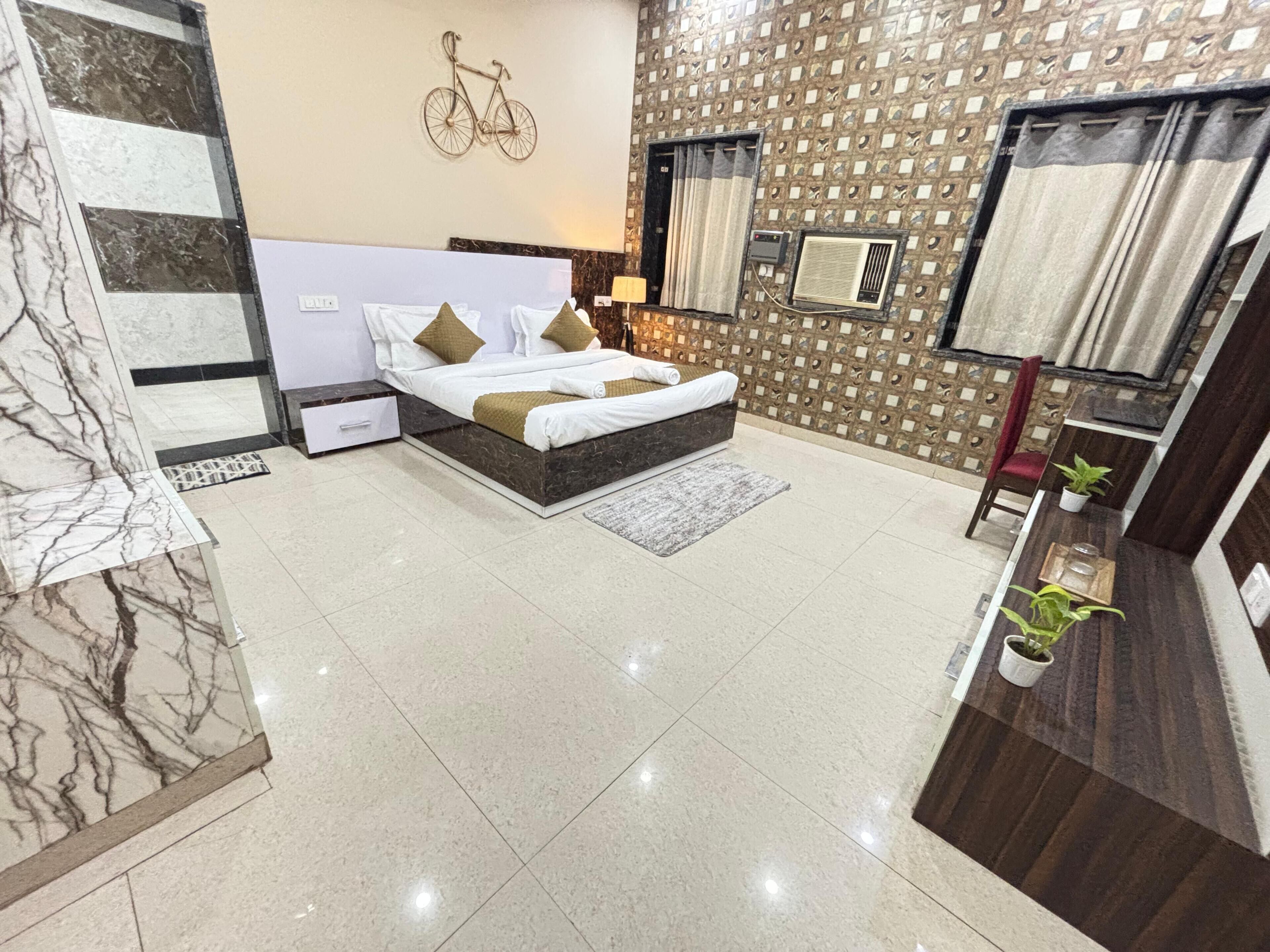 Un dormitorio moderno con suelo de mármol, una cama con ropa de cama blanca y cojines decorativos, una bicicleta decorativa colgada en la pared, un equipo de aire acondicionado y una pequeña planta en maceta.