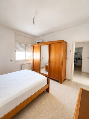 Ein Schlafzimmer mit Bett, Kleiderschrank und Blick zur Küche.