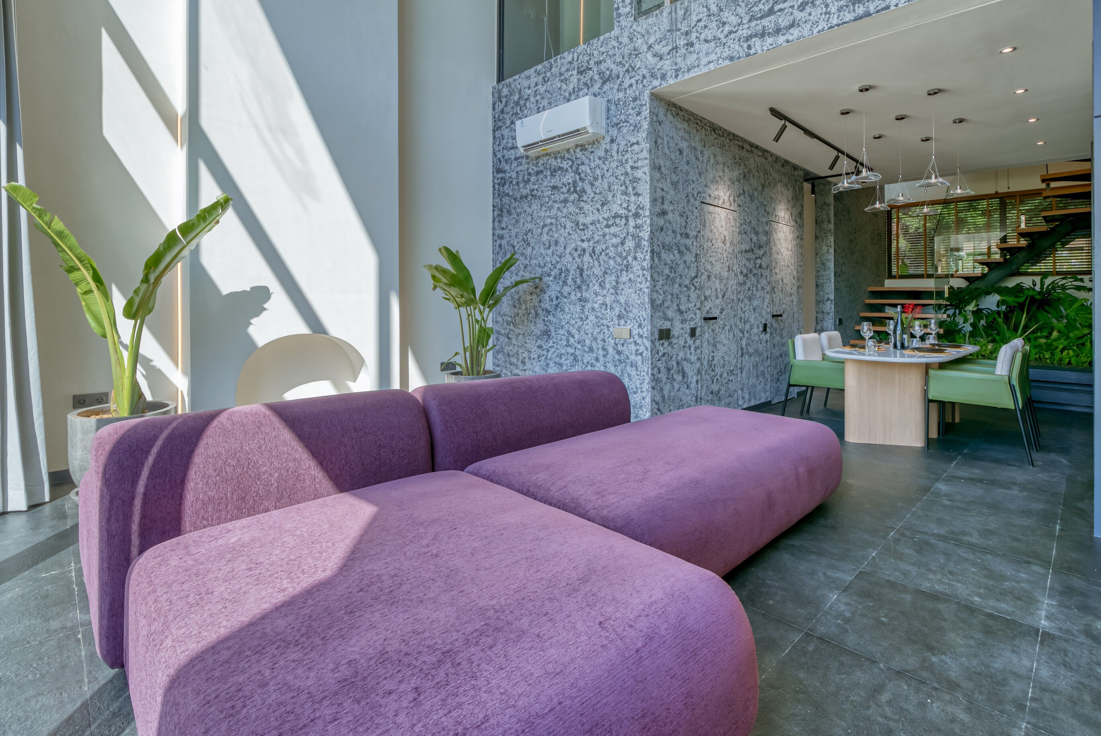 A modern living area with a purple sofa, a dining table with chairs, and potted plants.