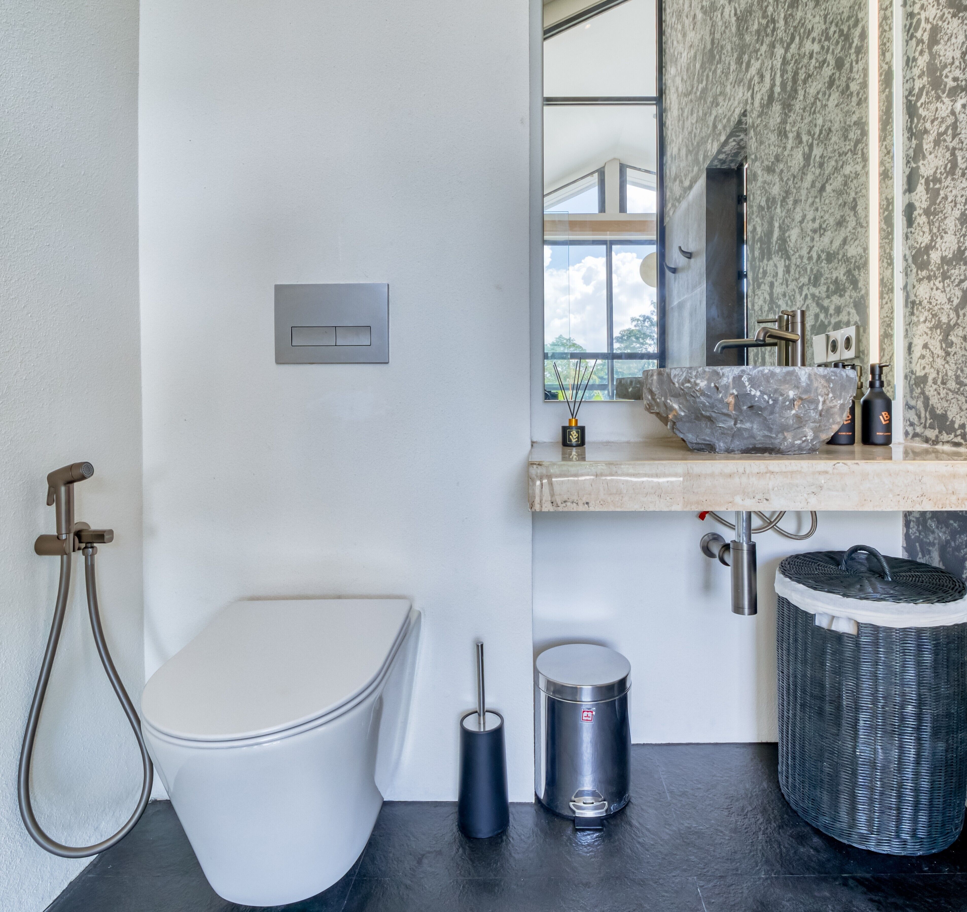 A modern bathroom with a white toilet, a large stone sink, a bidet, and a trash can.