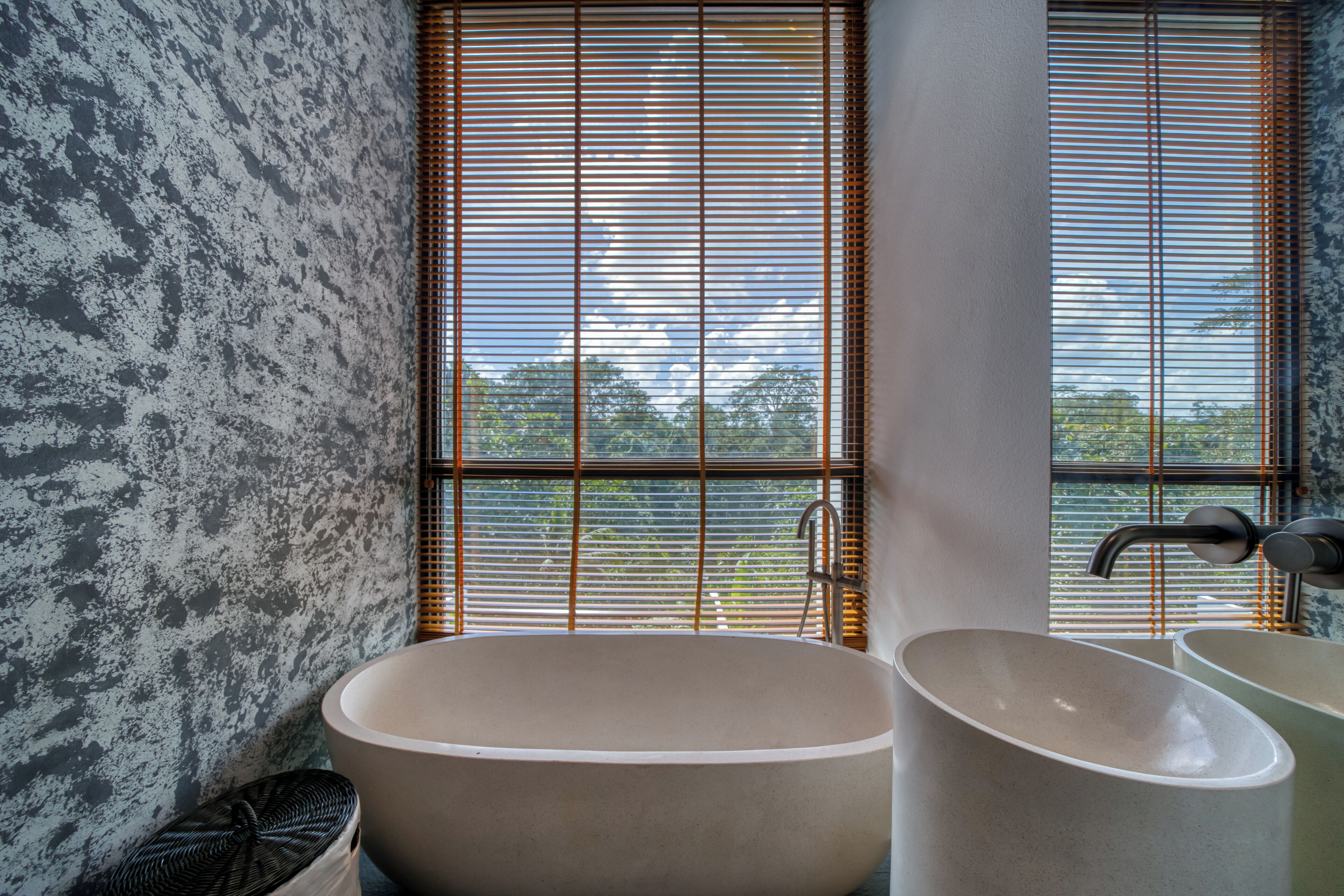 Ein Badezimmer mit einer freistehenden Badewanne, einem Waschbecken und einem Fenster mit Jalousien.