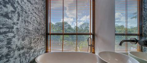 Ein Badezimmer mit einer freistehenden Badewanne, einem Waschbecken und einem Fenster mit Jalousien.