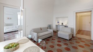 Een ruime zithoek met een bank, fauteuil en salontafel. Er is een keuken met een aanrecht en een koelkast. De vloer heeft een geometrisch patroon.