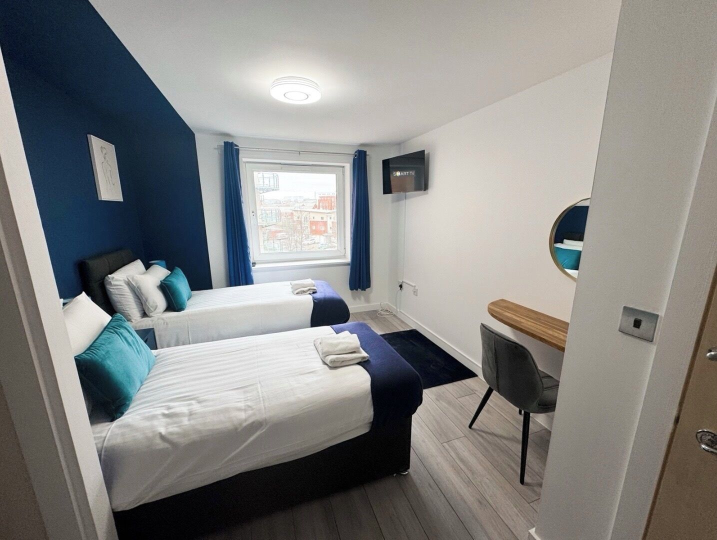 Een moderne hotelkamer met twee bedden, een bureau, een stoel, een televisie en een raam met gordijnen.