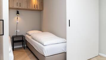 Un dormitorio pequeño y ordenado con una cama individual, una mesita de noche, una lámpara y armarios de madera sobre la cama.