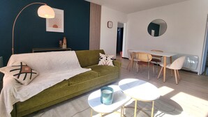 A modern living room with a green sofa, a white coffee table, and a dining area with a wooden table and chairs. - Waterfront 200m from beach (Royan)