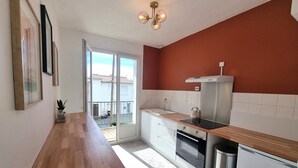 A modern kitchen with a wooden countertop, stainless steel appliances, and a sliding glass door leading to a balcony. - Waterfront 200m from beach (Royan)
