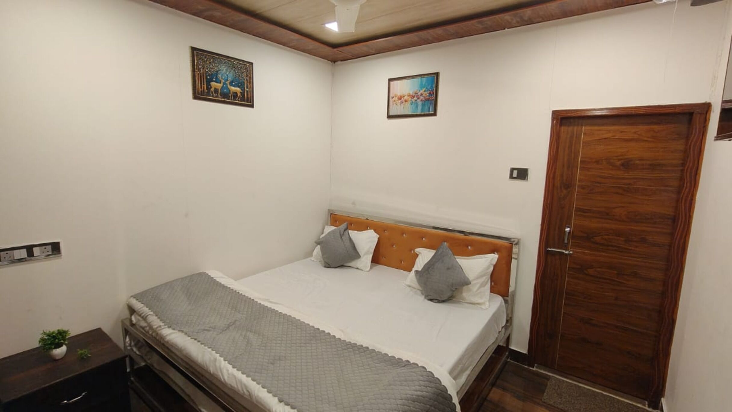 A bedroom with a bed, a wooden door, and two framed pictures on the wall.