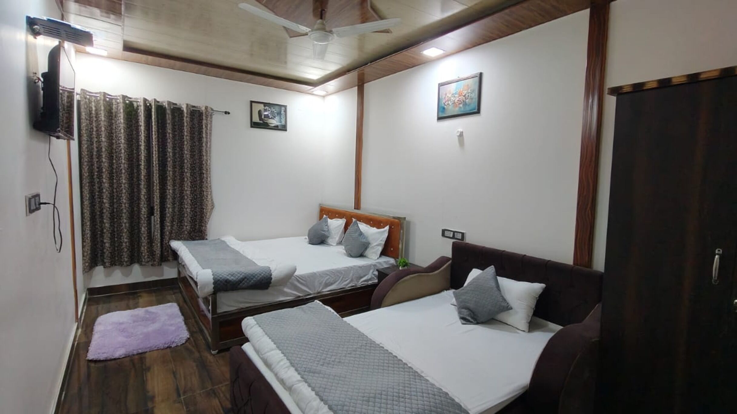 A bedroom with two single beds, a wooden floor, a ceiling fan, and a door.