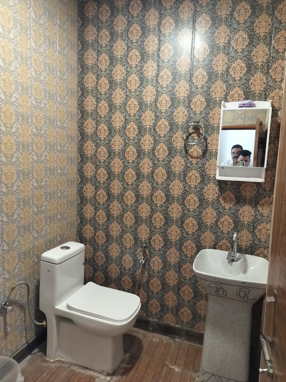 Ein Badezimmer mit gemustertem Wandpapier, einer Toilette, einem Waschbecken und einem Spiegel.