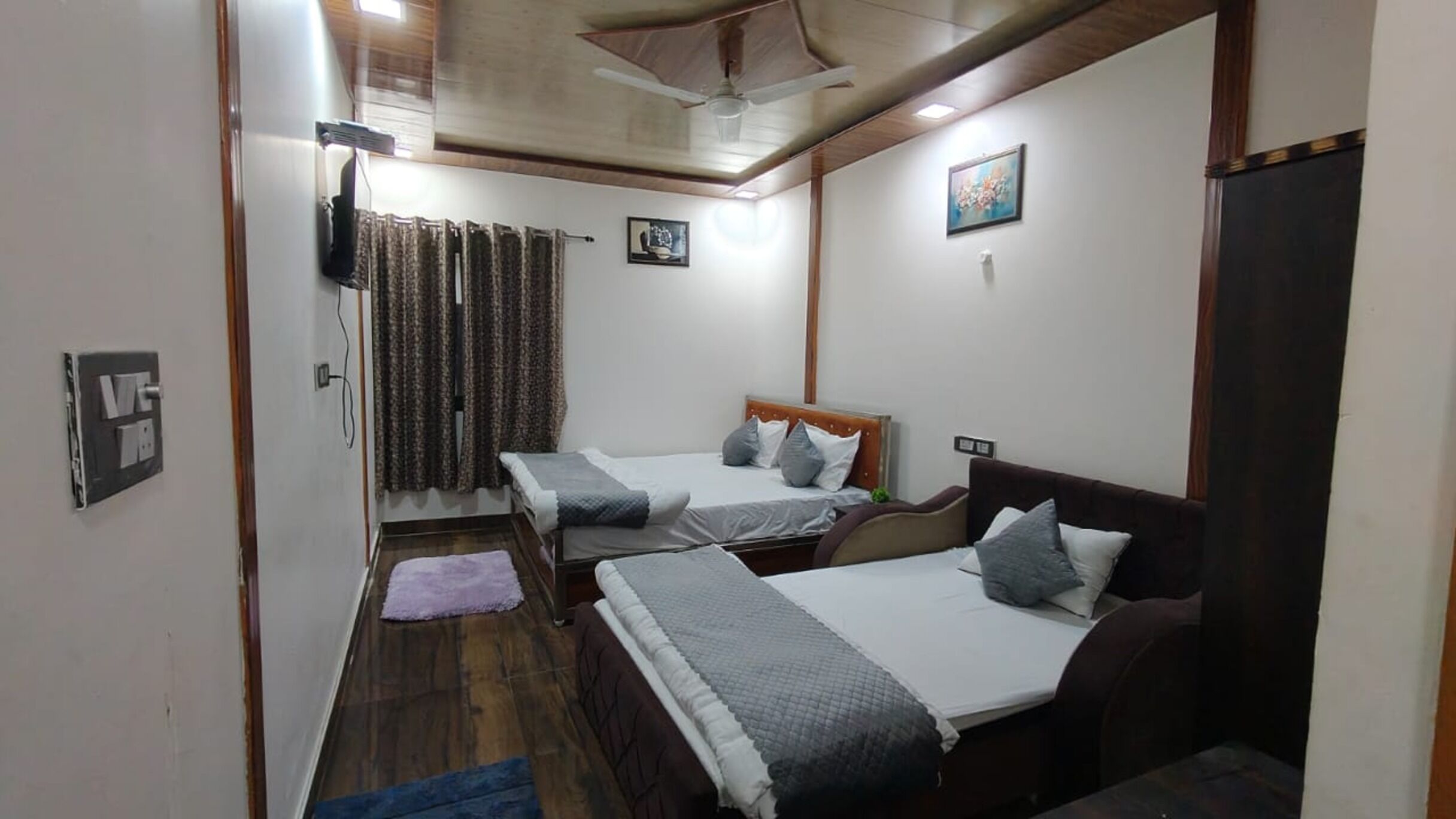 A compact room with two single beds, a ceiling fan, and a small window with curtains.