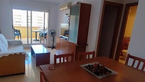 Een woonkamer met een bank, een eettafel met stoelen, een televisie en een ventilator.