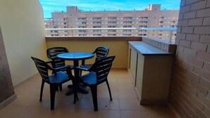 Een klein balkon met een ronde tafel en vier stoelen, een bakstenen muur, en een uitzicht op een woongebouw op de achtergrond.