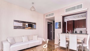 A modern living room with a glass coffee table, white sofa, and dining area with chairs. - Bellavista-Striking-1Bedroom with Annex (Dubai)