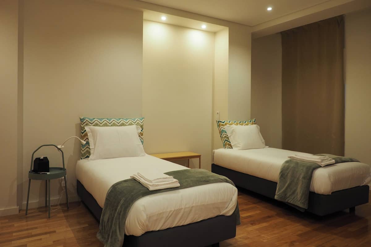 A hotel room with two beds, a small table, and a chair.