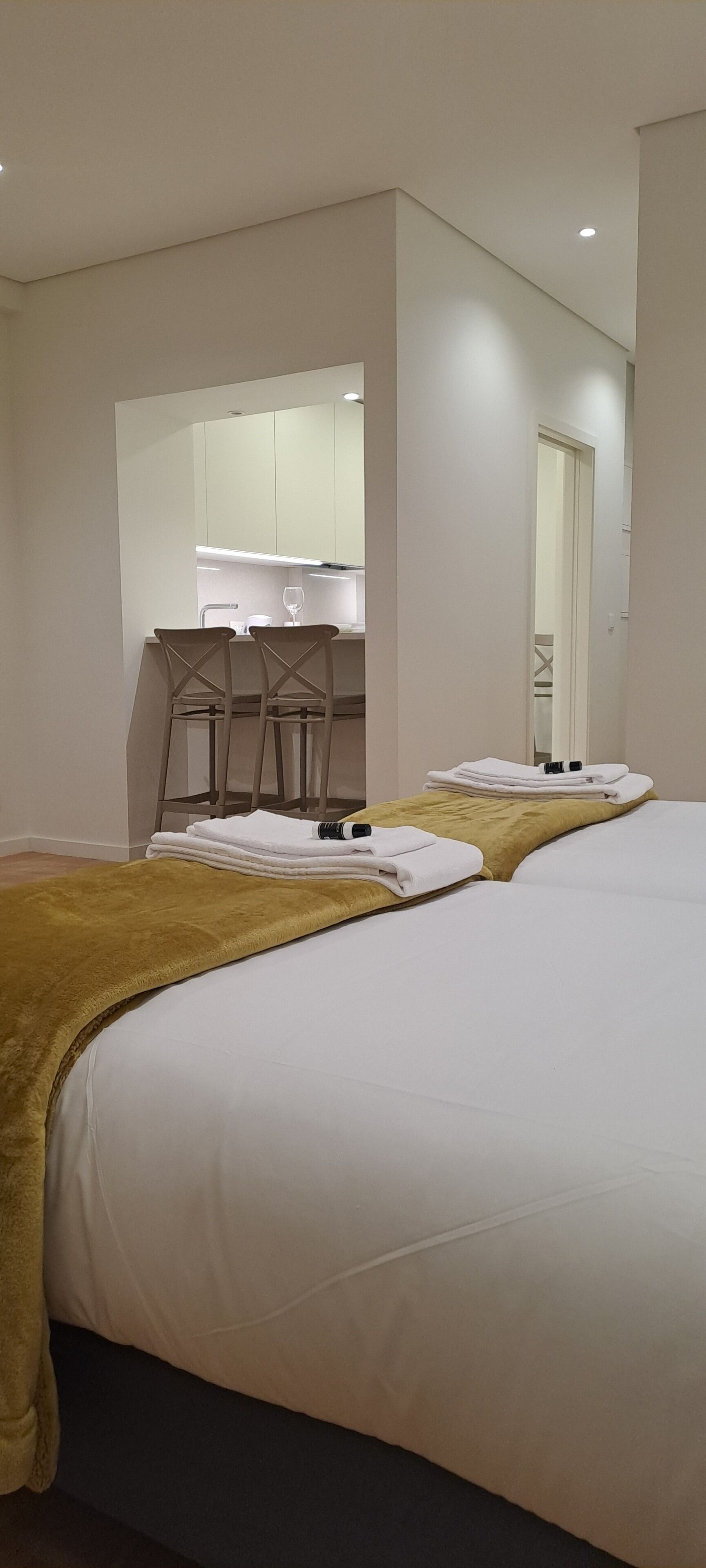 A hotel room with two beds, a kitchen area, and a bathroom.