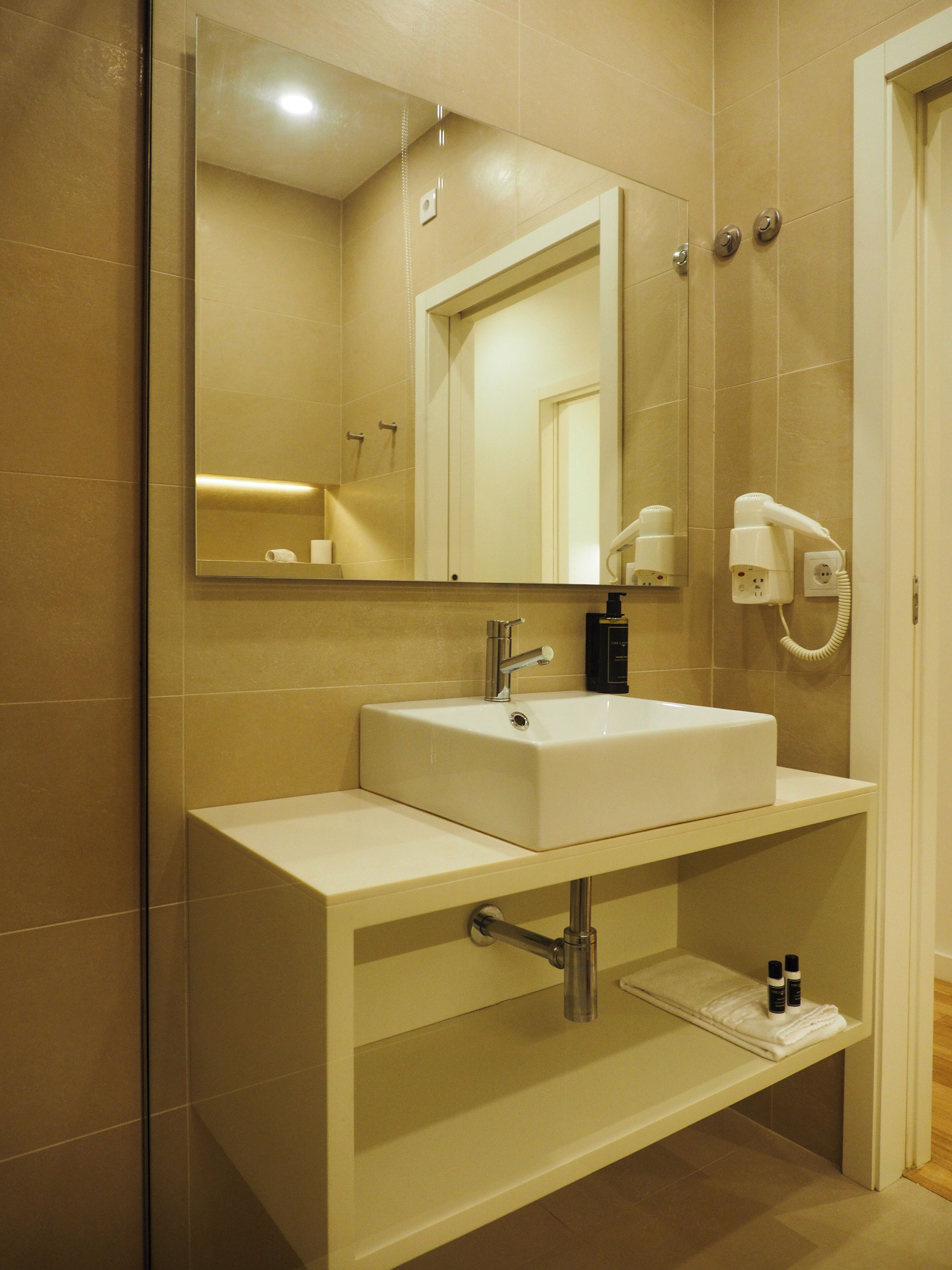 A bathroom with a white sink, a mirror, and a hairdryer on the wall.