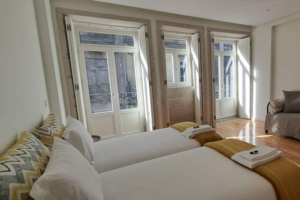 A hotel room with two beds, a sofa, a TV, and large windows.