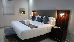 A neatly made bed with pillows and a bedside table with a lamp and phone. - Dikukama Executive Hotel (Tshabong)