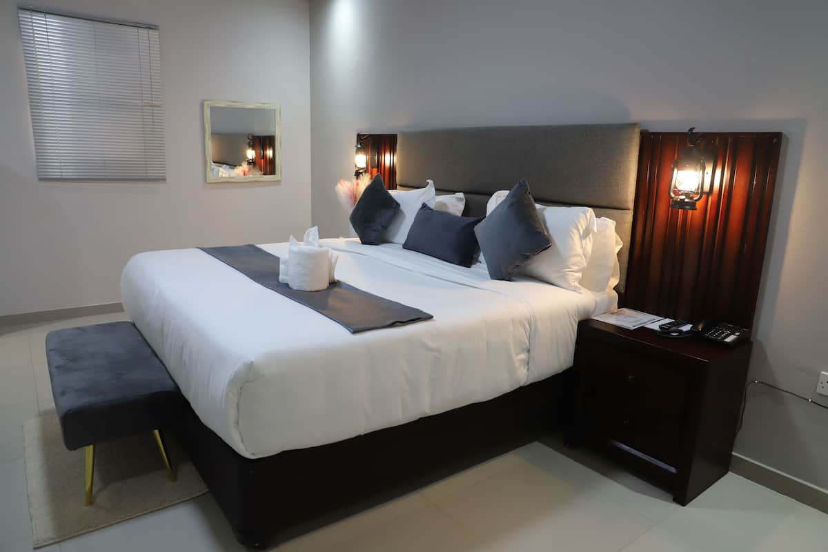 Cama bem arrumada com almofadas e mesa de cabeceira com abajur e telefone.