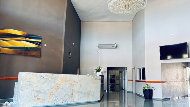 A modern lobby with a marble reception desk, a chandelier, a flat-screen TV, and a large artwork on the wall. - Dikukama Executive Hotel (Tshabong)