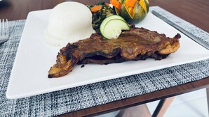 A plate with ribs, white rice, and a side salad on a table. - Dikukama Executive Hotel (Tshabong)