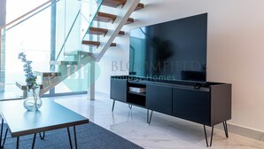Una sala de estar moderna con un televisor de pantalla plana grande, una escalera de cristal y un diseño minimalista.