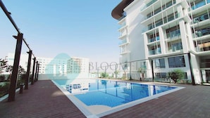 Un hotel moderno con piscina, varios pisos y cielo despejado.