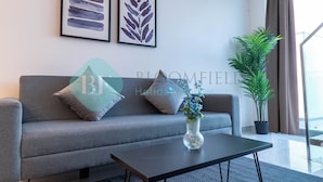 Una sala de estar moderna con un sofá gris, dos cuadros enmarcados, un florero con flores y una planta en maceta.