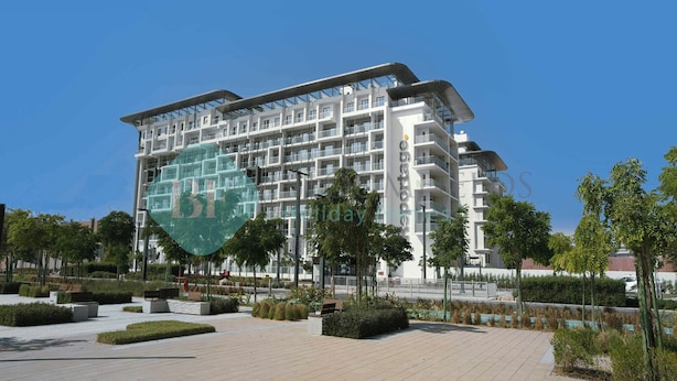 Un hotel moderno de varios pisos con techo plano y balcones, rodeado de jardines ajardinados y un camino pavimentado.