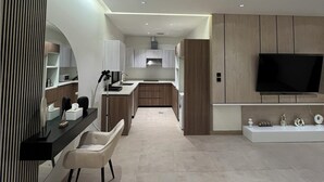 Una cocina moderna con una isla central, un comedor con sillas, un televisor montado en la pared y un cubo de basura.