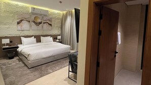 Un dormitorio moderno con una cama grande, un escritorio y un baño visible a través de una puerta abierta.