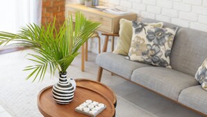 A living room with a grey sofa, a wooden coffee table with a striped vase and a small plant, and a brick wall in the background. - SCOTTS RETREAT - RELAX BY THE POOL (Scotts Head)
