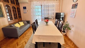 A furnished living room with a sofa, dining table, chairs, a TV, and a clock on the wall. - Apartman Niko (Crikvenica)