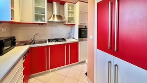 A modern kitchen with red and white cabinetry, stainless steel appliances, and a tiled backsplash. - Apartman Niko (Crikvenica)