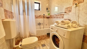 A bathroom with a toilet, washing machine, bathtub, and a shower curtain. - Apartman Niko (Crikvenica)