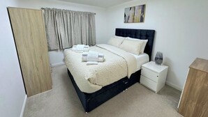 Un dormitorio ordenado con cama, mesita de noche y velador.