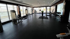 A gym with various exercise equipment, large windows, and a black floor. - Luxury Seaview Studio Apartment - RAK Al Marjan Island (Ras Al-Khaimah)