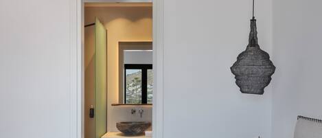 Een moderne badkamer met een grote spiegel, een wastafel op voet en een hangende lamp.