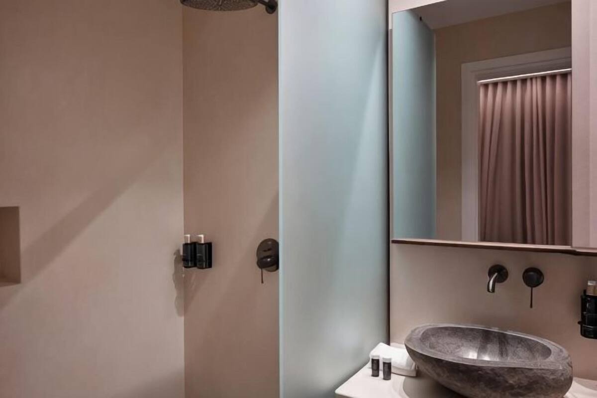 A bathroom with a stone sink, a mirror, and a shower.