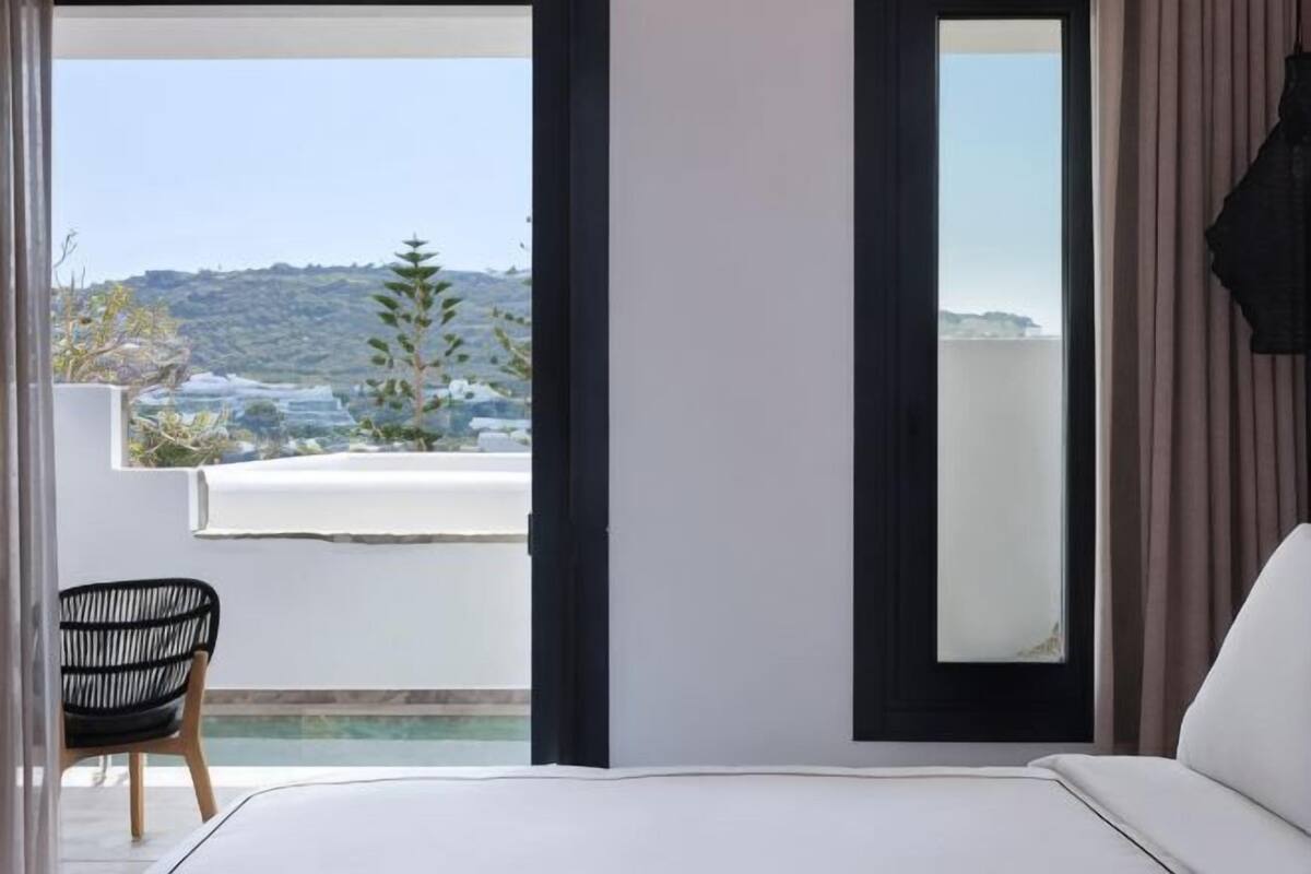 A bedroom with a bed, a chair, and a view of a balcony with a pool.